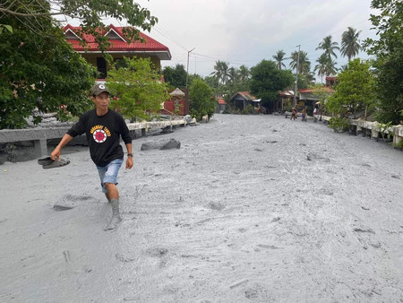 噴火中のカンラオン山から流れ出た火山泥流で埋め尽くされた道路を歩く住人＝５日、フィリピン・ネグロス島（環境天然資源省地方事務所提供）