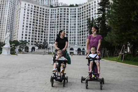 ベビーカーに赤ちゃんを乗せ、マンションの前を歩くベトナムの女性=2022年8月、ハノイ(AFP時事)