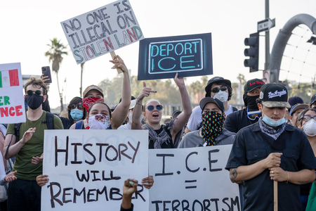 不法移民の取り締まりにデモ隊が抗議する中、プラカードを掲げる人たち=8日、米ロサンゼルス(AFP時事)