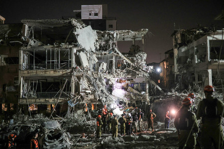 13日、イスラエルのテルアビブ近郊で、イランからのミサイル攻撃を受け、活動する救助隊員ら(ロイター時事)