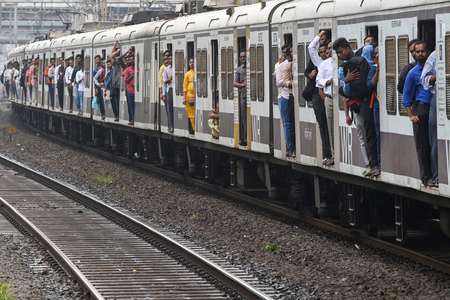 開けっ放しのドアから多くの乗客が身を乗り出している近郊電車=2022年9月、インド・ムンバイ(AFP時事)