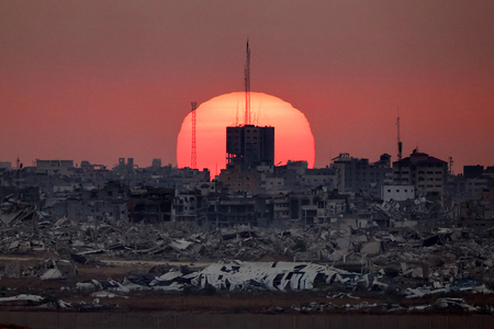 破壊された建物の背後に沈む夕日＝１日、イスラエルとパレスチナ自治区ガザの国境からパレスチナ側を撮影（ＡＦＰ時事）