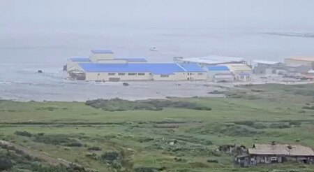 ３０日、千島列島のパラムシル島セベロクリリスクの海岸沿いの建物に押し寄せる津波（ＳＮＳの映像より）（ロイター時事）
