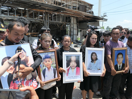 カンボジア軍の砲弾で炎上したタイのコンビニの前で、死亡した家族の写真を持つ遺族ら=1日、東北部シーサケート県