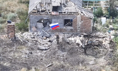 7月31日、ウクライナ東部ドネツク州チャシフヤールで、戦闘により破壊された建物の前に立ち、ロシア国旗を振る兵士=ロシア国防省が公開した映像より(EPA時事)