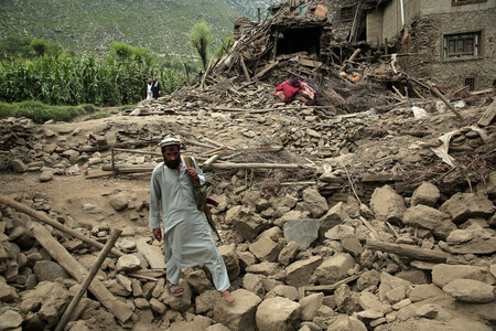 １日、アフガニスタン東部クナール州で、地震で損壊した家屋の横を歩く男性（ＥＰＡ時事）