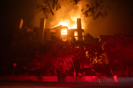 米カリフォルニア州ロサンゼルスのパシフィックパリセーズ地区で発生した山火事で、住宅から上がる炎=1月9日(AFP時事)
